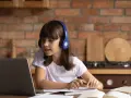 Dziewczynka w słuchawkach uczy się z laptopem. Jej liceum online to przyszłość edukacji.