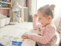 Mała dziewczynka z zapałem uczy się literek dla 3 latka. Na biurku ma kolorowanki z alfabetem i flamastry.