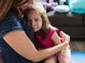 Mała dziewczynka płacze, wtulona w mamę. To właśnie parenting – trudne chwile i bezwarunkowa miłość.