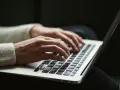 Dłonie piszą na klawiaturze laptopa, czy przed tym stawiamy przecinek? Praca zdalna w pełnym skupieniu.