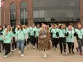 Grupa młodych ludzi w zielonych koszulkach z napisem "Szkoła w chmurze przedmioty" idzie przed budynkiem.