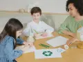 Dzieci i nauczycielka tworzą scenariusz zajęć "z ekologią na ty". Na stole symbol recyklingu, żarówki i globus.