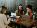 Trzy kobiety śmieją się przy laptopach, pracując nad wspólnym projektem. To idealna prasówka z WOS-u, pełna pozytywnej energii i współpracy.