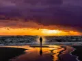 Samotna postać na plaży podczas burzowego zachodu słońca. Promienie przebijające się przez chmury i fale morza symbolizują sposób, jak wyładować złość.