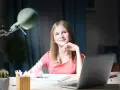Uśmiechnięta dziewczynka z długopisem w dłoni, zastanawia się nad zadaniem. Obok laptop, dlatego jaka to część mowy?
