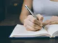 Dłoń pisze długopisem w notatniku, planując ile argumentów w rozprawce będzie potrzebnych do przekonania czytelnika.