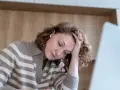 Kobieta z trudnościami z koncentracją opiera głowę na dłoni, patrząc w dół.