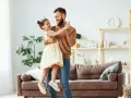 Uśmiechnięty ojciec i córka w koronie tańczą w salonie. Radosna chwila między tatą a jego małą księżniczką.