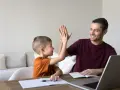 Ojciec i syn dają sobie piątkę, świętując sukcesy w nauce. To chwila radości, kiedy nie stawiamy przecinka, bo wszystko jest jasne.