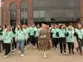 Grupa młodych ludzi w zielonych koszulkach idzie przed budynkiem. Jak się dostać do szkoły w chmurze? Zapytaj ich!