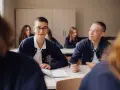 Uczniowie liceum podczas lekcji. Chłopiec w okularach uśmiecha się, a jego kolega pisze w zeszycie. To obraz nauczania domowego liceum.