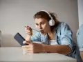 Młoda kobieta w słuchawkach je płatki, patrząc w telefon. Czy to objawy fonoholizmu?