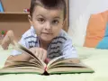 Chłopiec leży na łóżku z otwartą książką. To świetny sposób, jak zachęcić dziecko do czytania.