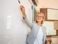 Nauczycielka z uśmiechem wskazuje markerem na tablicę, przygotowując wniosek o dokonanie oceny pracy nauczyciela.