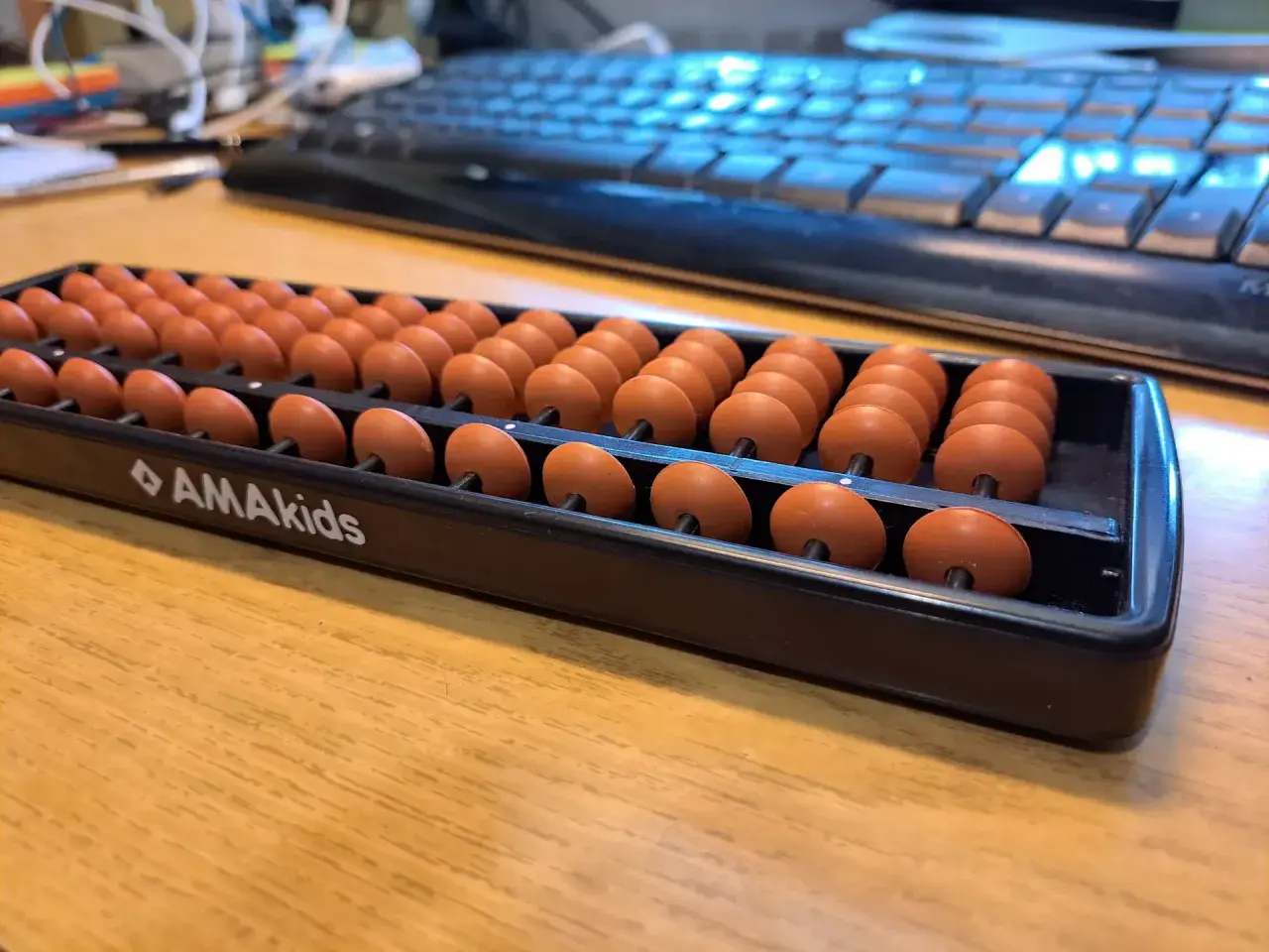 Zestaw koralików do arytmetyki mentalnej AMAkids na drewnianym biurku, obok klawiatury.