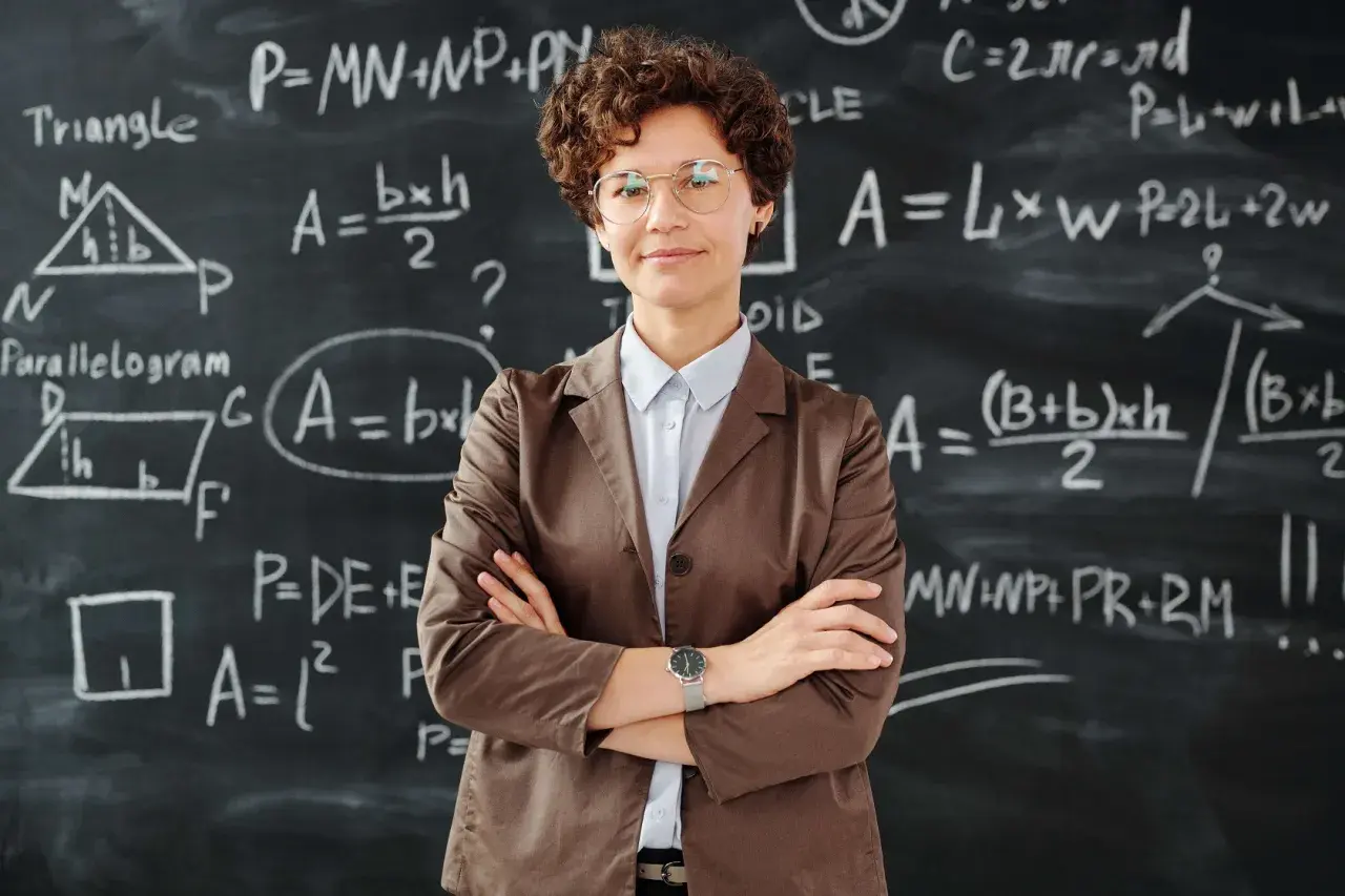 Nauczycielka z okularami na tle tablicy z równaniami matematycznymi. To obraz edukacji w Norwegii, gdzie nauka jest priorytetem.