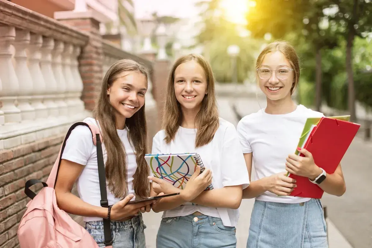 Trzy uśmiechnięte uczennice z zeszytami i teczkami. Czy w 7 klasie jest plastyka? Pewnie tak, skoro mają tyle materiałów!