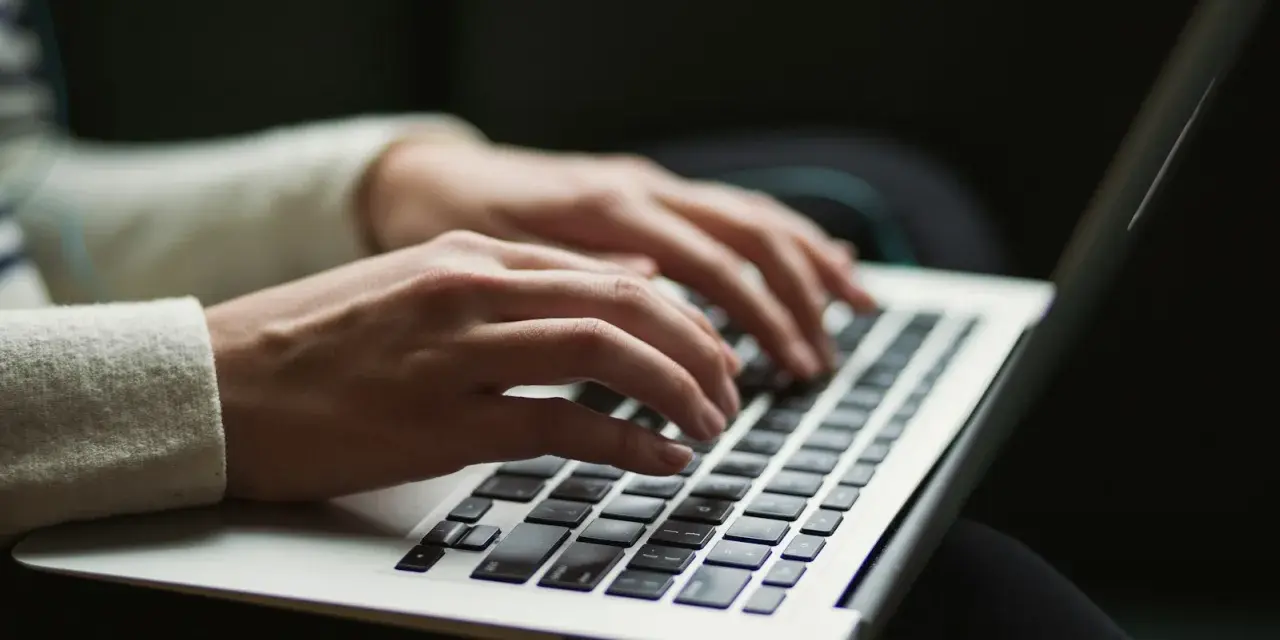 Dłonie piszą na klawiaturze laptopa, czy przed tym stawiamy przecinek? Praca zdalna w pełnym skupieniu.