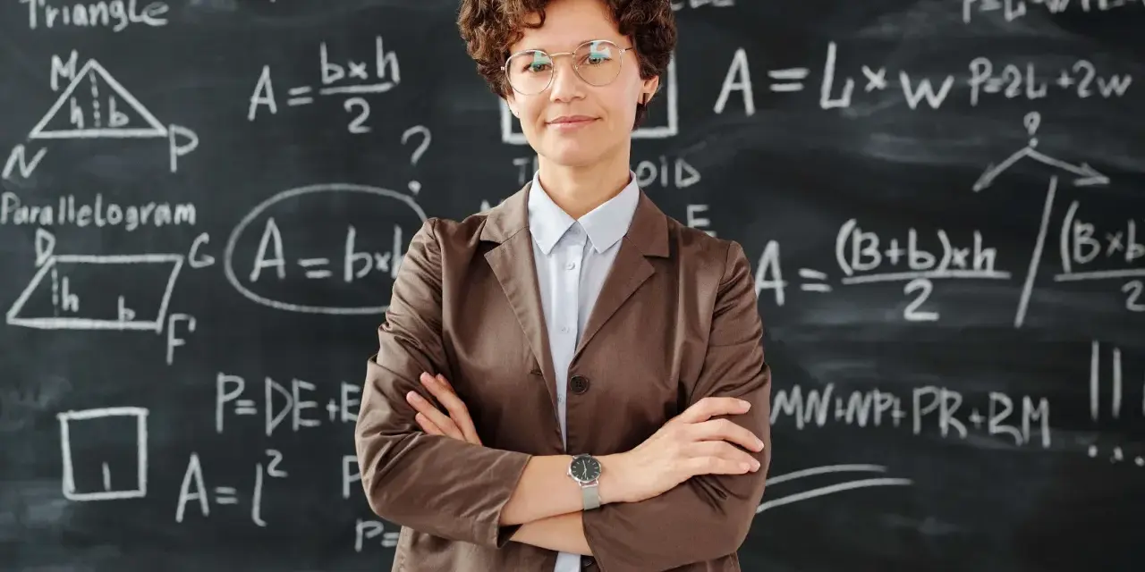 Nauczycielka z okularami na tle tablicy z równaniami matematycznymi. To obraz edukacji w Norwegii, gdzie nauka jest priorytetem.