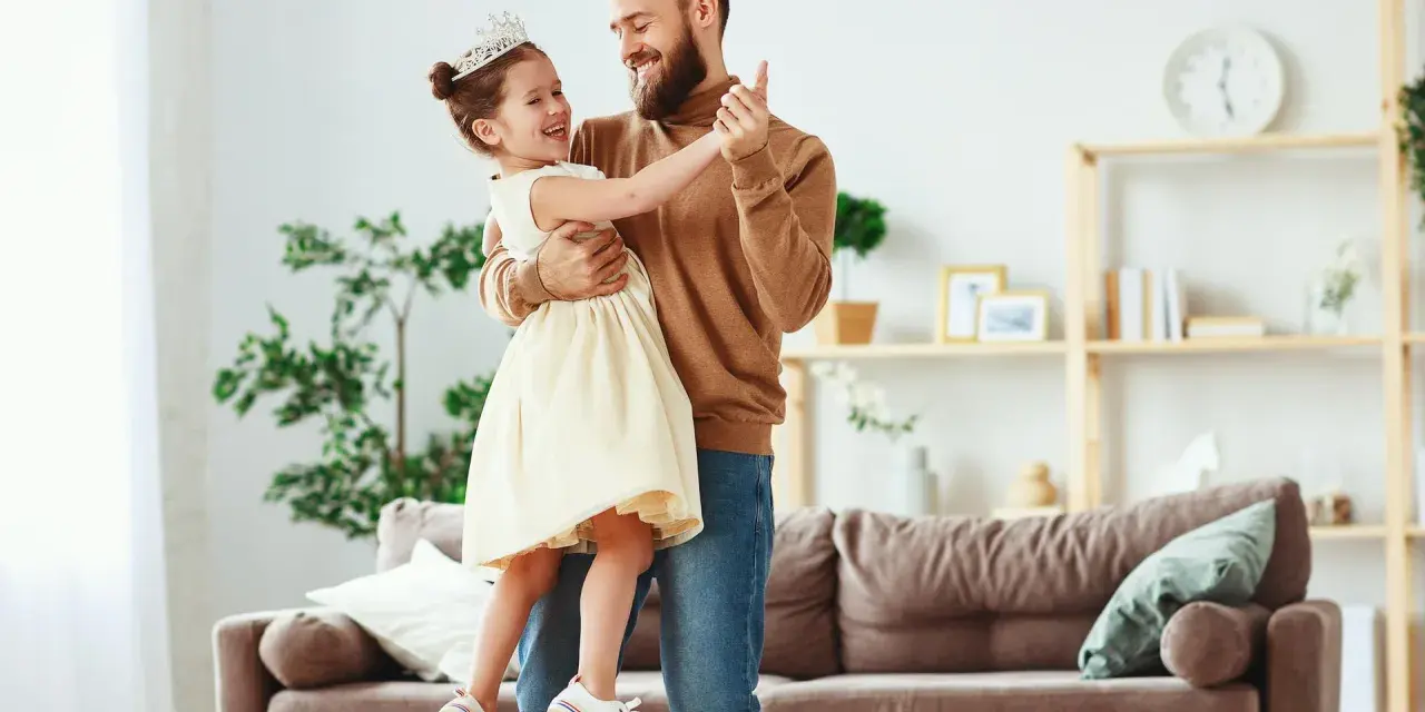 Uśmiechnięty ojciec i córka w koronie tańczą w salonie. Radosna chwila między tatą a jego małą księżniczką.