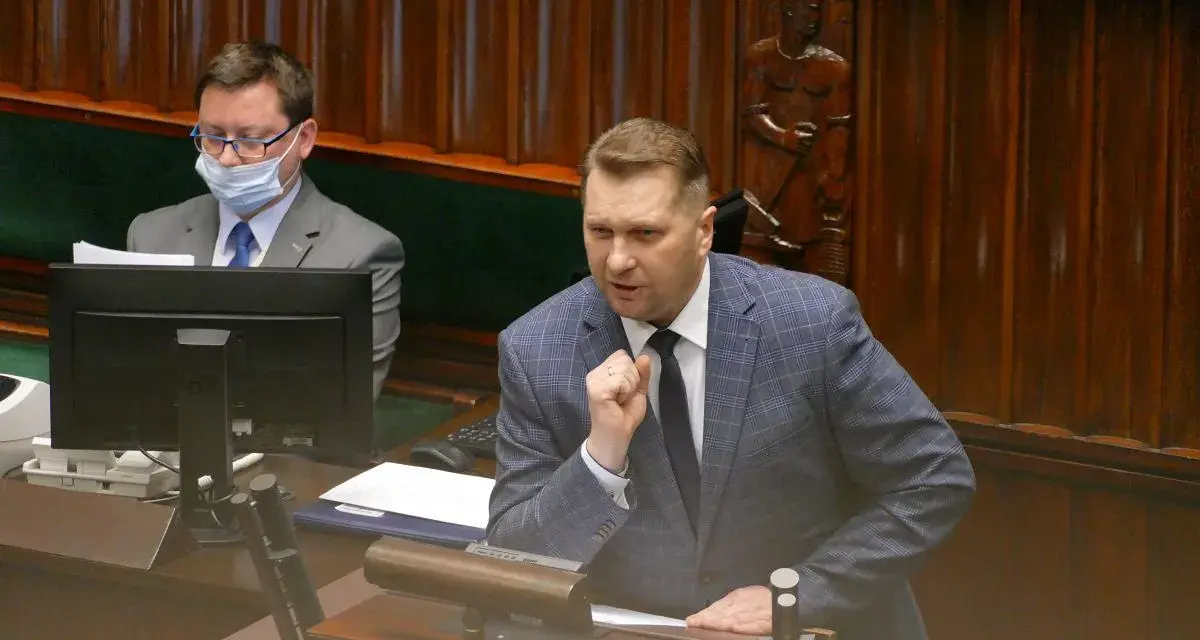 Poseł przemawia, dyskutując o tym, lex czarnek co zmienia. W tle siedzi inny poseł w masce.