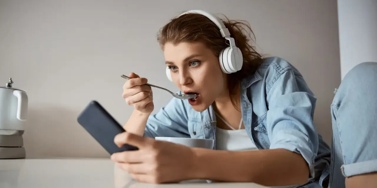 Młoda kobieta w słuchawkach je płatki, patrząc w telefon. Czy to objawy fonoholizmu?