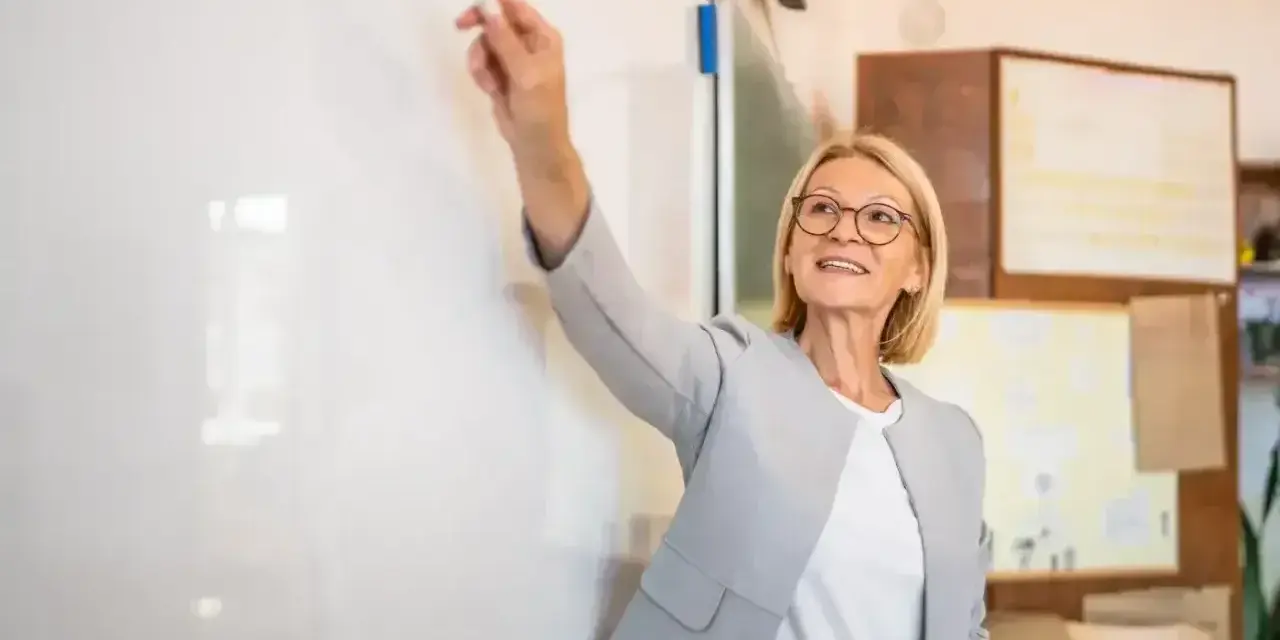 Nauczycielka z markerem przy tablicy, uśmiechnięta. To może być ocena pracy nauczyciela początkującego, który właśnie prezentuje swoje umiejętności.