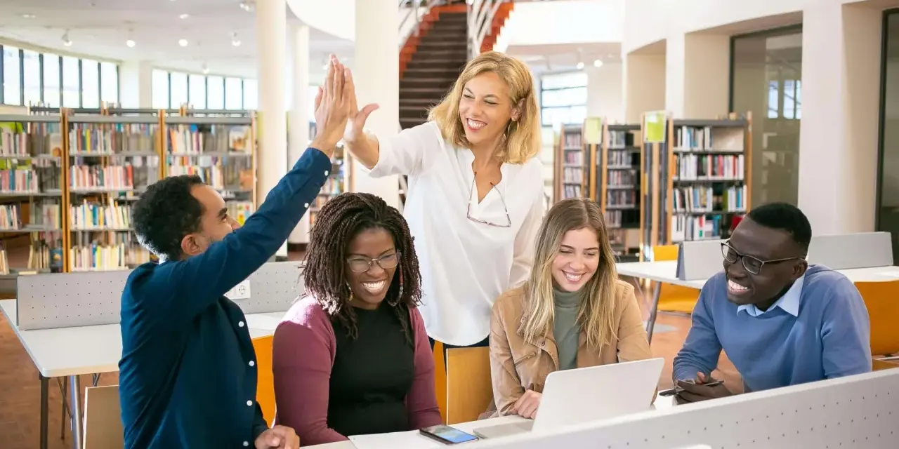 Uśmiechnięta grupa studentów i nauczycielki świętują sukces w bibliotece. To obraz nowoczesnej edukacji w Australii.