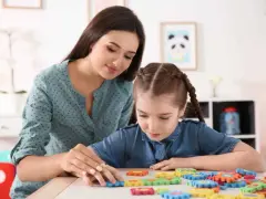 Terapeuta pomaga dziecku z niepełnosprawnością intelektualną w stopniu lekkim układać kolorowe puzzle.