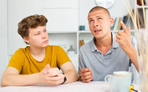 Ojciec tłumaczy synowi, jak rozmawiać z nastolatkiem. Chłopak słucha uważnie, a mężczyzna gestykuluje, podkreślając swoje słowa.