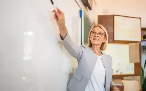 Nauczycielka z markerem przy tablicy, uśmiechnięta. To może być ocena pracy nauczyciela początkującego, który właśnie prezentuje swoje umiejętności.