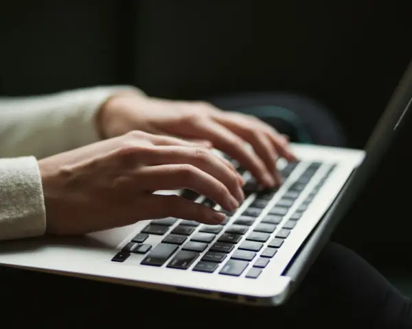 Dłonie piszą na klawiaturze laptopa, czy przed tym stawiamy przecinek? Praca zdalna w pełnym skupieniu.