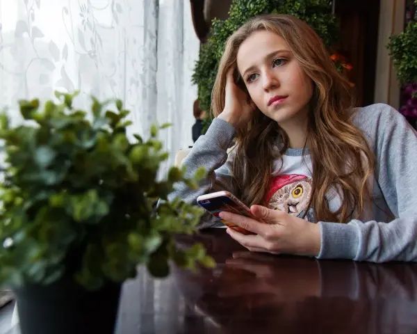 Dziewczyna z telefonem w dłoni, zamyślona, przeżywa trudny czas dojrzewania.