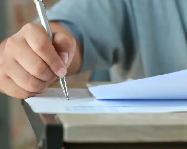 Dłoń trzymająca długopis, która wypełnia test. Czy przed jak również stawiamy przecinek, gdy piszemy.