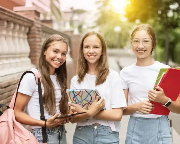 Trzy uśmiechnięte uczennice z zeszytami i teczkami. Czy w 7 klasie jest plastyka? Pewnie tak, skoro mają tyle materiałów!