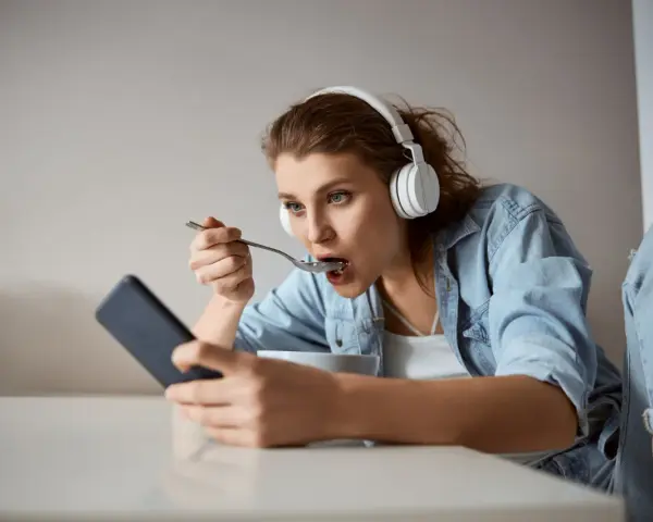 Młoda kobieta w słuchawkach je płatki, patrząc w telefon. Czy to objawy fonoholizmu?