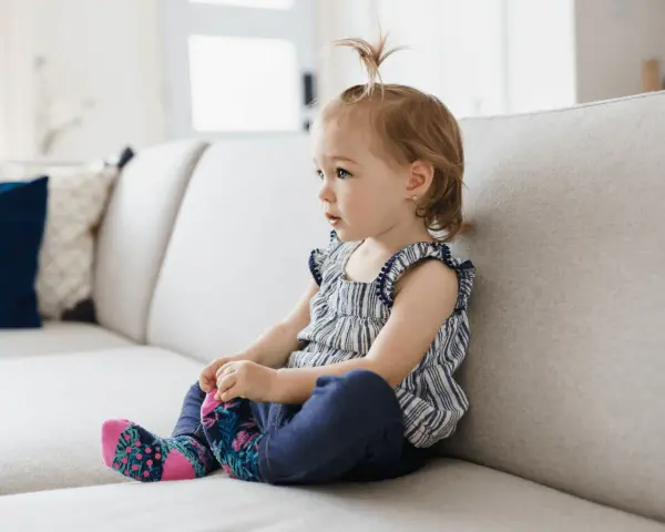 Mała dziewczynka siedzi na kanapie, wyrażając różne emocje, jak w filmie edukacyjnym dla dzieci.