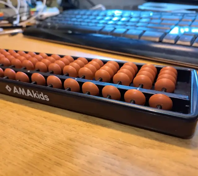 Zestaw koralików do arytmetyki mentalnej AMAkids na drewnianym biurku, obok klawiatury.