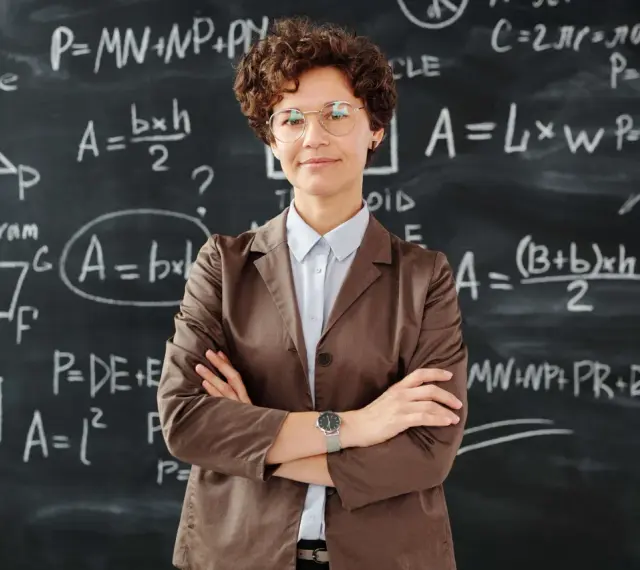 Nauczycielka z okularami na tle tablicy z równaniami matematycznymi. To obraz edukacji w Norwegii, gdzie nauka jest priorytetem.