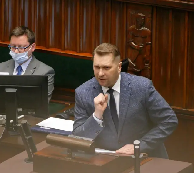 Poseł przemawia, dyskutując o tym, lex czarnek co zmienia. W tle siedzi inny poseł w masce.