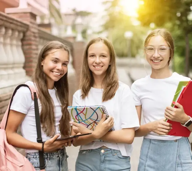 Trzy uśmiechnięte uczennice z zeszytami i teczkami. Czy w 7 klasie jest plastyka? Pewnie tak, skoro mają tyle materiałów!