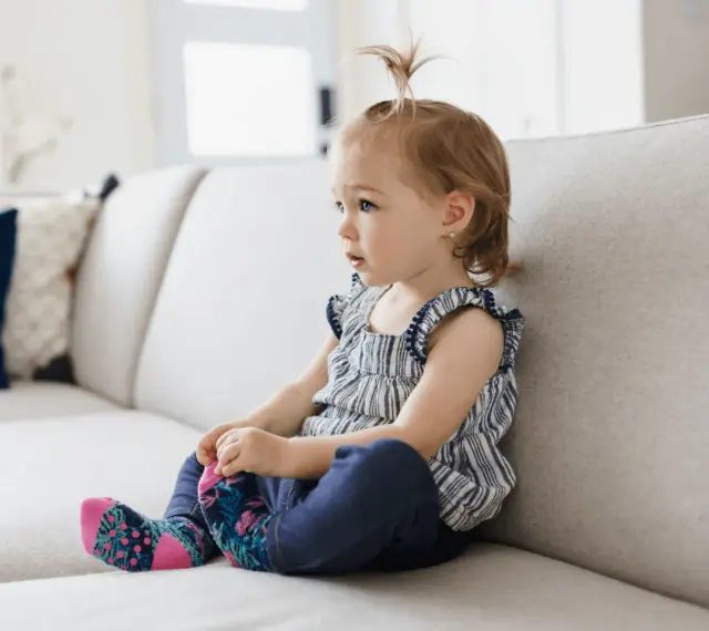 Mała dziewczynka siedzi na kanapie, wyrażając różne emocje, jak w filmie edukacyjnym dla dzieci.