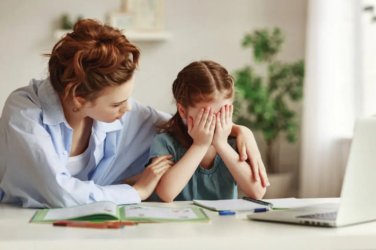 Smutne dziecko zakrywa twarz dłońmi, mama pociesza je, szukając wsparcia, gdy dziecko nie chce chodzić do szkoły.