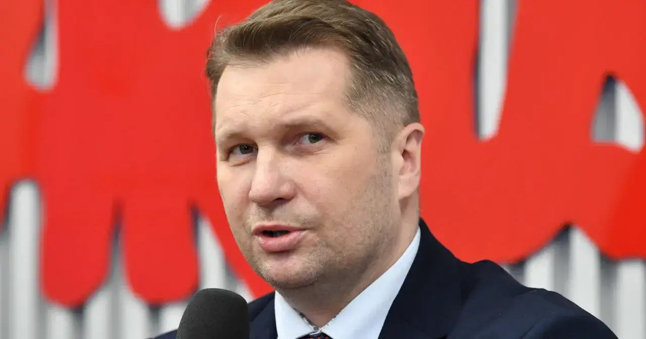 Przemysław Czarnek mówi o tym, lex czarnek co zmienia w edukacji. Mężczyzna w garniturze na tle czerwonego logo.