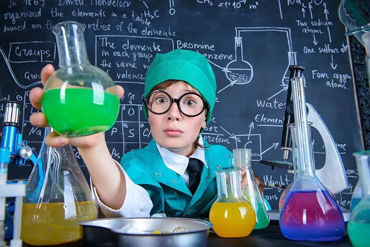 Mały chemik w okularach i czepku przygotowuje spektakularne eksperymenty dla dzieci, trzymając zielony płyn.