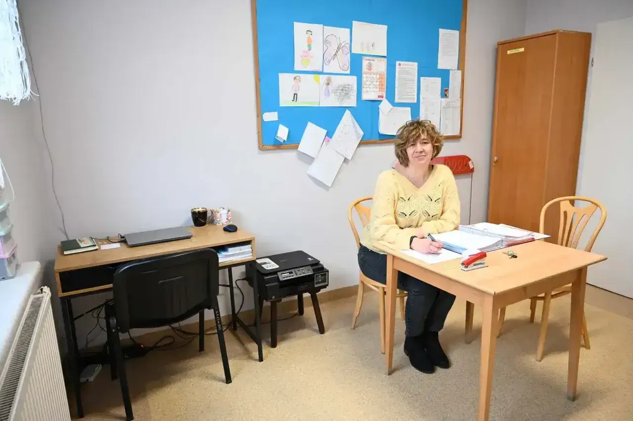 Pedagog szkolny przy biurku, na tablicy rysunki dzieci. Czy etat pedagoga szkolnego a liczba uczniów to wyzwanie?