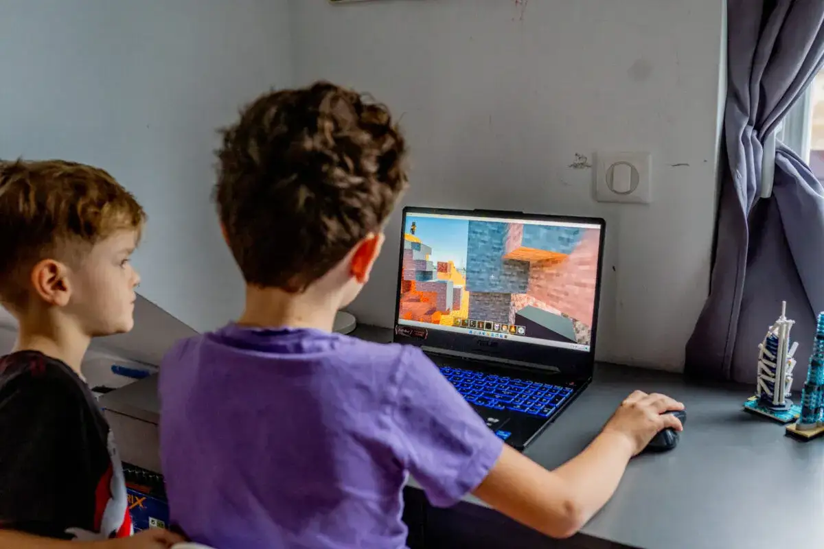 Dwóch chłopców gra w Minecrafta na laptopie. Gra jest odpowiednia dla dzieci od najmłodszych lat, rozwijając kreatywność.