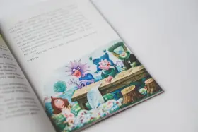 Smok Luomił i tajemnice złości. Ilustracja z książki przedstawia wesołe stworki przy stole, a obok nich dziewczynkę.