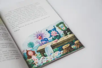 Smok Luomił i tajemnice złości. Ilustracja z książki przedstawia wesołe stworki przy stole, a obok nich dziewczynkę.
