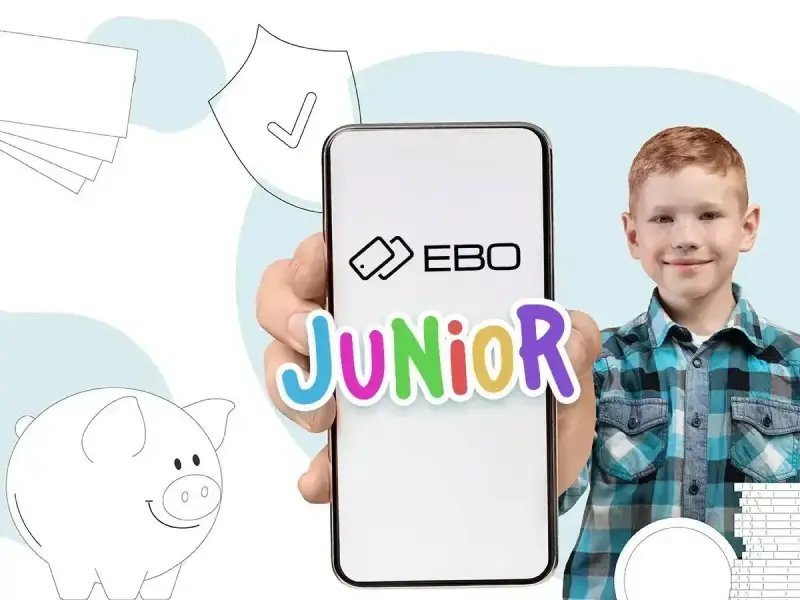Chłopiec z uśmiechem trzyma telefon z napisem EBO Junior. Obok świnka skarbonka i stos banknotów. Idealne rozwiązanie na kieszonkowe dla 18 latka.